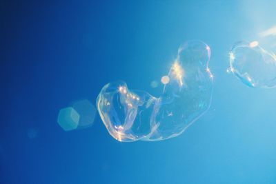 Low angle view of bubbles against blue sky on sunny day