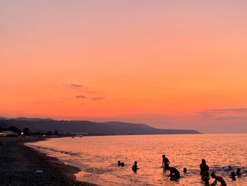 Silhouette people on beach against orange sky