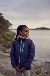 Smiling girl standing at beach against sky