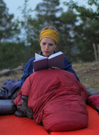 Female hiker reading book while sitting in bed on field