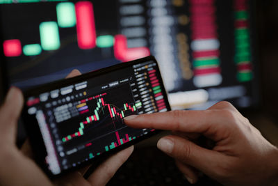 Hand of young business girl looking at trading graphs on office computer and mobile phone