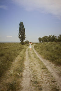Rear view of person walking on road amidst field against sky
