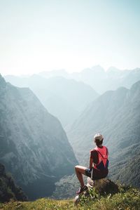 Man sitting on mountain looking at mountains against sky