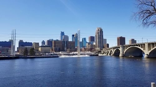 Bridge over river by buildings against clear blue sky