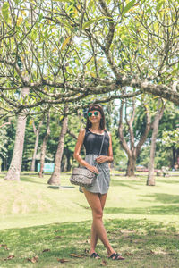 Full length portrait of woman standing by tree