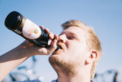 Close-up portrait of man holding beer bottle against sky
