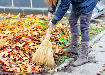 Low section of woman cleaning autumn leaves by sidewalk