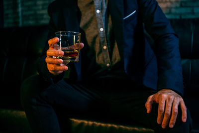 Midsection of man drinking glass while sitting on table