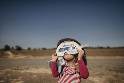 Girl holding solar eclipse glasses and mask while standing against sky