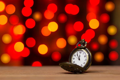 Close-up of pocket watch against illuminated christmas lights