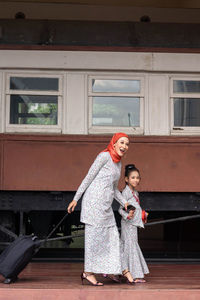 Full length of mother and girl standing against building