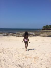 Rear view of woman in bikini walking on sand at beach