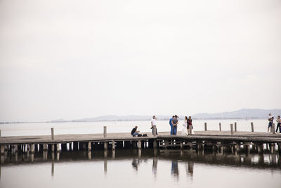 People standing on pier over sea against clear sky