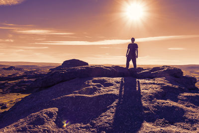 Man standing on rock against sky during sunset