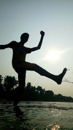 Silhouette man jumping in water at sunset