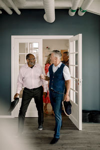 Multiracial senior men talking while carrying shoes and entering dance class