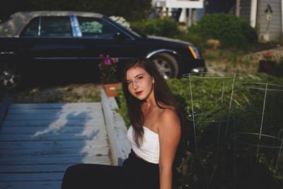 Portrait of beautiful woman sitting on retaining wall against car