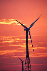Low angle view of wind turbine against orange sky