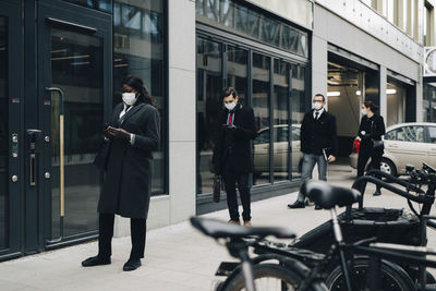 Business people maintaining social distancing while standing on footpath by building in city