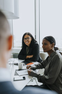 Smiling senior businesswoman sitting by female colleague in board room during meeting