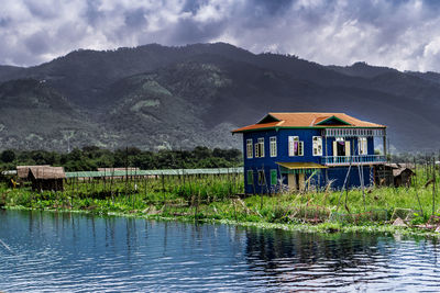 House by lake and mountains against sky