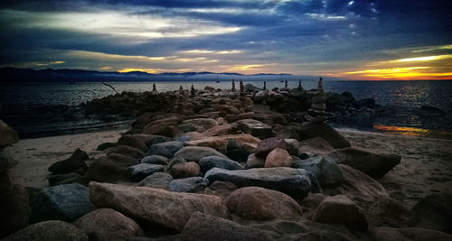 Rocks on beach against sky during sunset