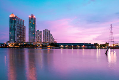 Illuminated city by sea against sky at dusk