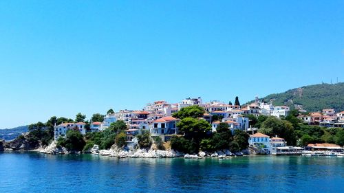 Houses by sea against clear blue sky