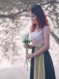 Beautiful young woman with flowers standing against trees