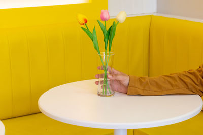 Midsection of person holding yellow flower vase on table