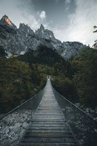 Footbridge leading towards mountains against sky