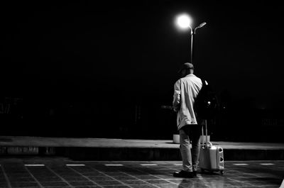 Rear view of man standing on illuminated street at night