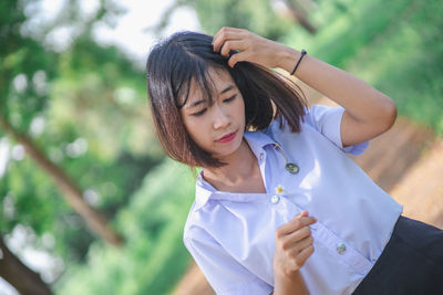 Young woman with hand in hair standing at park