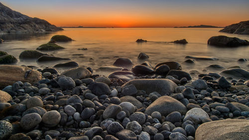 Rocks on beach against sky during sunset