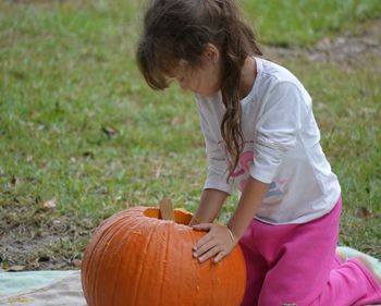 Girl carving pumpkin while kneeling on grassy field