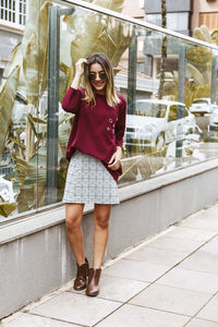 Smiling young woman standing on sidewalk by glass building