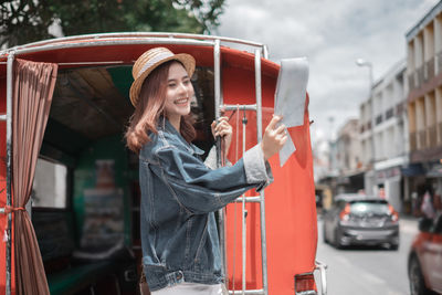 Young woman standing by car on street in city