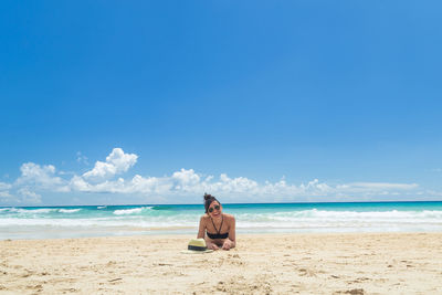 Rear view of woman sitting at beach against clear blue sky