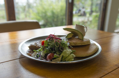 Close-up of pancakes with salad served in plate on wooden table