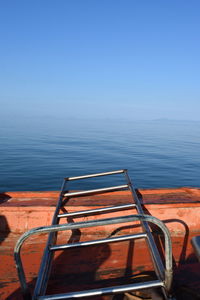 Metallic ladder on boat in sea against clear blue sky