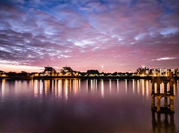 Scenic view of lake by illuminated buildings against sky during sunset