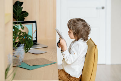 Rear view of boy holding table at home