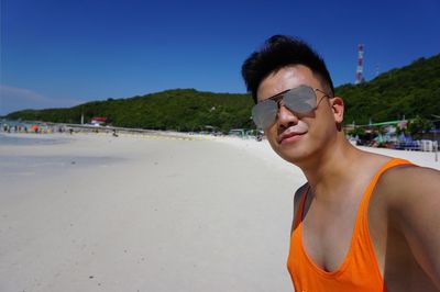 Portrait of young man wearing sunglasses while standing at beach