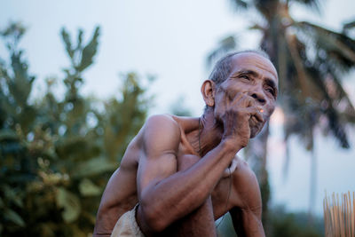 Portrait of shirtless man looking away outdoors