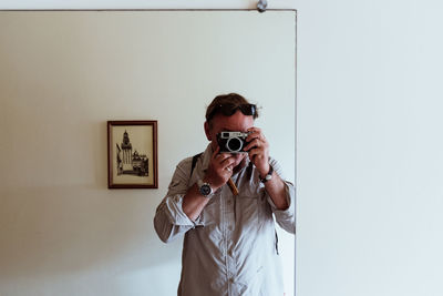 Man photographing with camera standing against wall