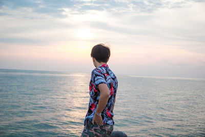 Boy standing in sea against sky during sunset