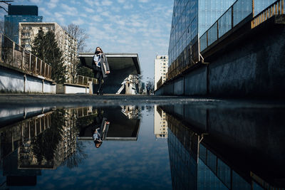 Reflection of man standing on puddle against buildings