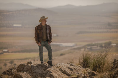 Portrait of adult man with cowboy hat standing on top of hill