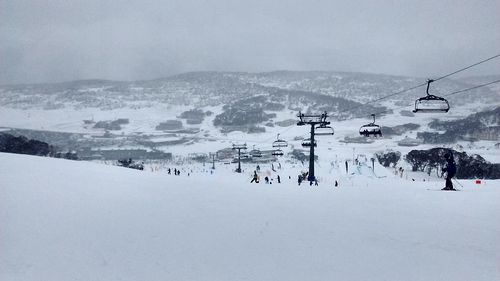 Ski lift over snow covered mountains against sky