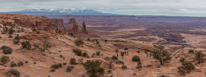 Panoramic view of tourists enjoying mesa arch with snow capped mountains in the background